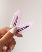 Person holding two Glow Recipe pink clips against beige background.
