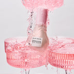 Pink skincare bottle with water droplets on a light gray background