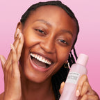 Woman holding a skincare product against a pink background