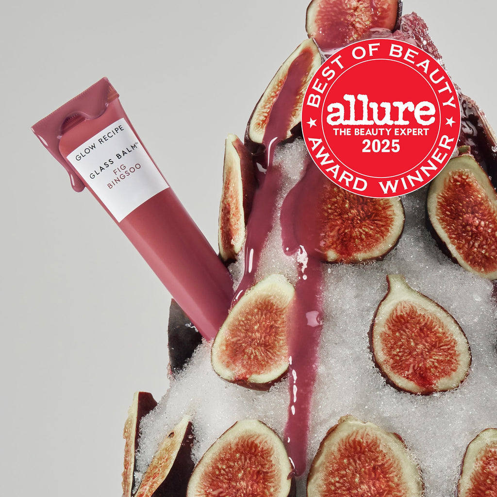 Glass Balm Lip Treatment tube standing upright in Fig Bingsoo, a sheer mauve-nude tinted lip balm, in a teaser shot.